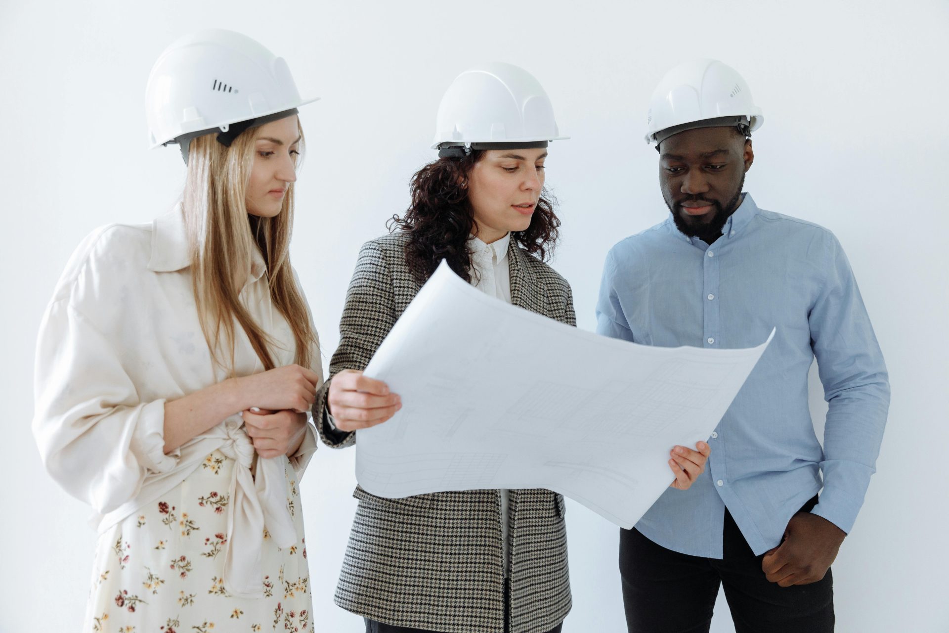 Three architects wearing hard hats reviewing blueprints indoors for a construction project.